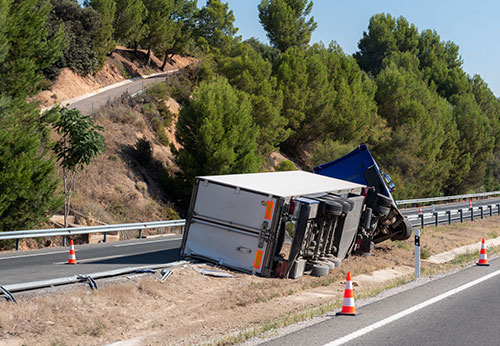 An overturned semi-truck is lying on the side of a winding road.